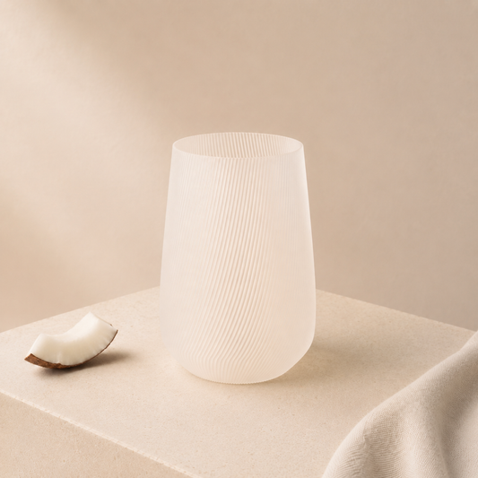 Vase Fjord Glow Coconut en bioplastique PLA blanc translucide avec rainures délicates, posé sur fond beige avec une noix de coco.
